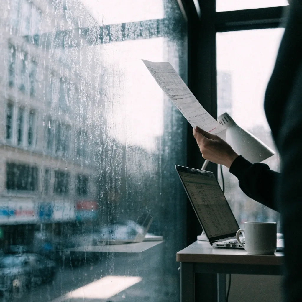 A paper receipt held between two fingers against a rain-streaked window